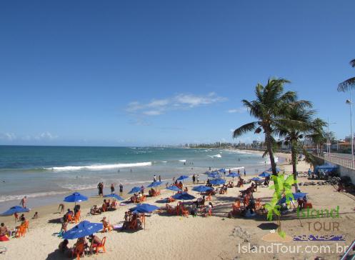 Praia de Itapuã - Salvador - Bahia - Vista da praia com pessoas tomando sol, banho de mar e sentados na areia, com mar a esquerda e coqueiros a direita